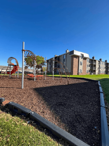A playground with a swing set and a play structure in front of a building.
